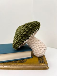 a knitted mushroom sitting on top of a book next to a stack of books