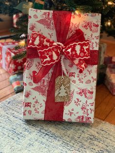 a present wrapped in red and white paper with a bow on it sitting under a christmas tree