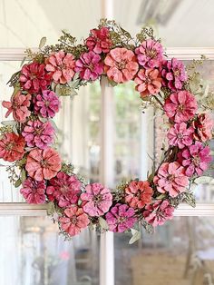 a wreath with pink flowers hanging from the side of a window in front of a door