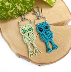 two crocheted owl keychains sitting on top of a wooden slice next to a plant