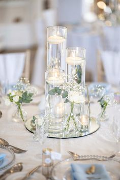 candles and flowers in glass vases on a white table cloth with silverware, plates and napkins