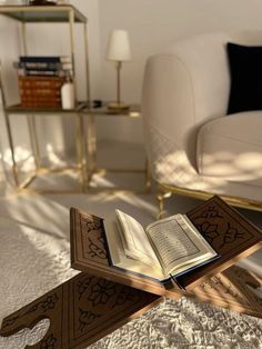 an open book sitting on top of a wooden table next to a white couch and chair