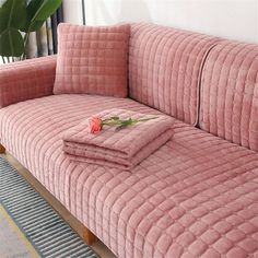 a pink velvet couch with matching pillows and blankets on it in front of a window