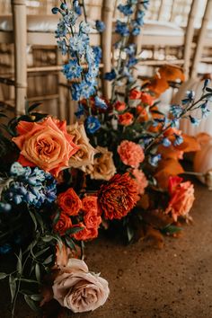 an arrangement of flowers on the ground in front of chairs at a wedding reception with blue and orange colors