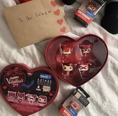 two heart shaped boxes with various items in them sitting on a white sheet next to a card