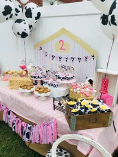 a table topped with lots of desserts next to a cow themed cake and balloons