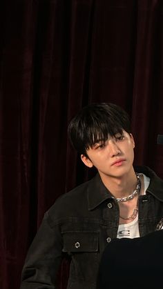 a young man with black hair and piercings sitting in front of a microphone on stage