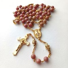 Miraculous Medal Rosary Rhodonite beads with gold bead caps. This beautiful, handcrafted Catholic Heirloom Rosary combines 6mm Rhodonite beads with a Miraculous Medal centerpiece and a Saint Benedict Crucifix. The Pater beads are Rose Bud Connectors. Dimensions & Specifications: Ave Beads: 6mm Rhodonite beads. Pater Beads: Rose Bud Connectors. Crucifix: The Saint Benedict Crucifix measures 1-1/2 Inches H. Center: The Miraculous Medal centerpiece measures 1-3/4 inch H. Length: The filigree rosary measures 20.5" long. Wire: 20-gauge 18 k gold plated wire. A gift for prayer and devotion. Comes in a gift box with a instructional prayer card on How to Pray the Rosary. * This rosary would make a great gift for your favorite Catholic undergoing Confirmation, Baptism, First Communion, or a Wedding Gold Hand-strung Spiritual Rosary, Gold Bohemian Rosary With 8mm Beads, Bohemian Gold Rosary With 8mm Beads, Praying The Rosary, Saint Benedict, Rose Bud, Miraculous Medal, The Saint, Prayer Cards