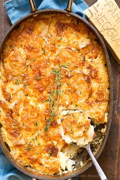 a casserole with cheese and herbs in a pan on a wooden table next to utensils