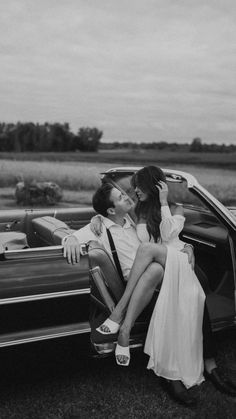 a man and woman sitting on the back of a convertible car in front of a field