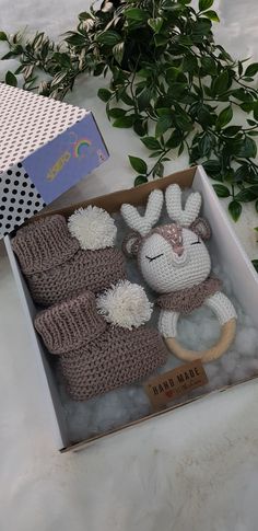 an open box with two knitted items in it on a white surface next to some green plants