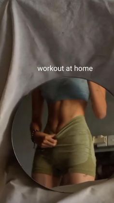 a woman in green shorts looking at her reflection in a mirror with the words workout at home written on it