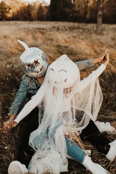 a person in a costume sitting on the ground next to a woman wearing a mask