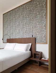 a bed with white sheets and pillows in a bedroom next to a wooden shelf on the wall