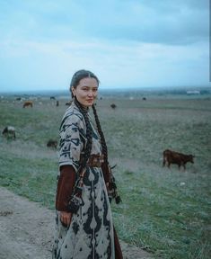 a woman standing in the middle of a field with cows grazing on the other side