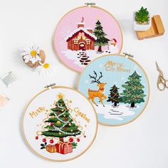 three cross - stitch christmas designs are displayed on a white surface with scissors and other crafting supplies