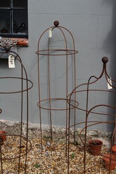 three metal plant stands with tags on them in front of a gray wall and window