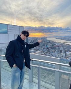 a man standing on top of a building next to a tall building with a sunset in the background