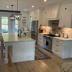 a kitchen with white cabinets and an island in the middle of the room is lit by pendant lights