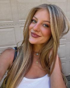 a woman with long blonde hair wearing a white tank top and gold cross pendant necklace