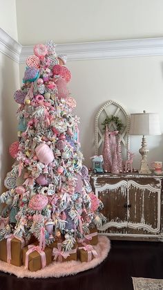 a decorated christmas tree with pink and white ornaments on it's top, in a living room