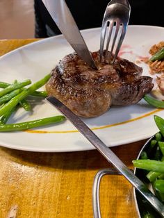 a fork is stuck into some meat on a plate with green beans and asparagus