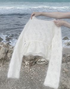 a woman is holding up a white sweater on the rocks by the water's edge