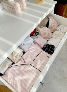 an open drawer on top of a white table filled with clothes and other items in it