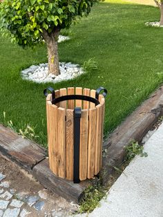 a wooden trash can sitting on the side of a road next to a green tree