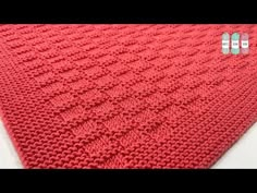 a red knitted blanket sitting on top of a white table next to two pins