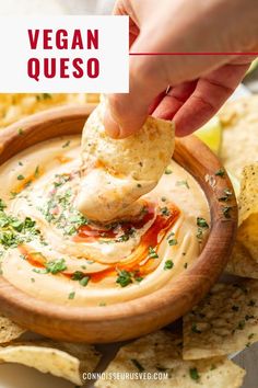 a hand dipping a tortilla chip into a bowl of vegan queso