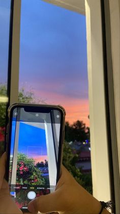 someone taking a photo with their cell phone in front of an open window at sunset