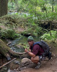 a man kneeling down next to a creek in the woods with a backpack on his back