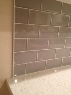 a white counter top sitting next to a wall with gray tiles on it's sides