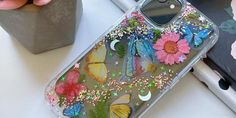 a phone case with butterflies and flowers on it sitting next to a flower potted plant