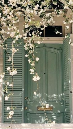 an open green door with white flowers growing on the outside and side of it, in front of a building