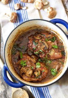 a blue pot filled with meat and mushrooms on top of a wooden table next to garlic