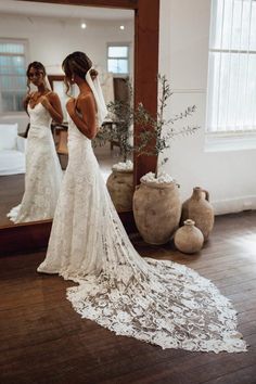 a woman standing in front of a mirror wearing a wedding dress and looking at her reflection