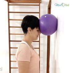 a woman holding a purple balloon in front of her face while standing next to a wall