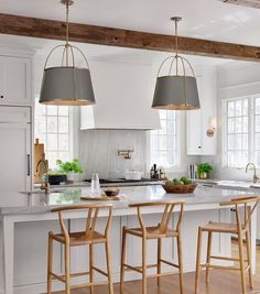 a kitchen with white cabinets and wooden stools in front of an island that has two pendant lights hanging over it