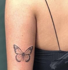 a small butterfly tattoo on the back of a woman's left arm and shoulder