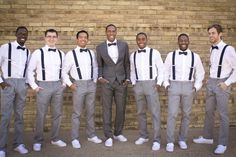 a group of men standing next to each other in front of a brick wall wearing suits and bow ties