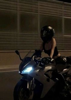 a woman riding on the back of a silver motorcycle at night with her helmet on