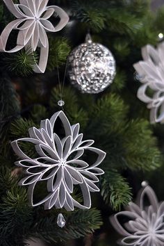 ornaments are hanging from the christmas tree in silver and white colors, including snowflakes