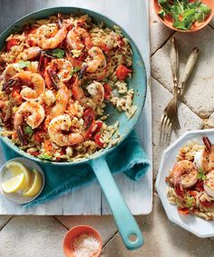 two plates with shrimp, pasta and lemon wedges next to each other on a table