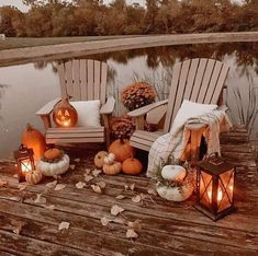 some chairs with pumpkins and candles on a wooden deck near water at night time