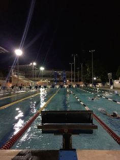 an empty swimming pool at night with people in the water and onlookers