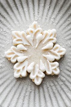 a close up of a white flower on a plate with sand and water droplets around it