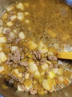 a pot filled with meat and potatoes on top of a blue stovetop next to a wooden spoon