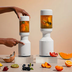 two blenders with fruits and vegetables on the table, one being squeezed into another